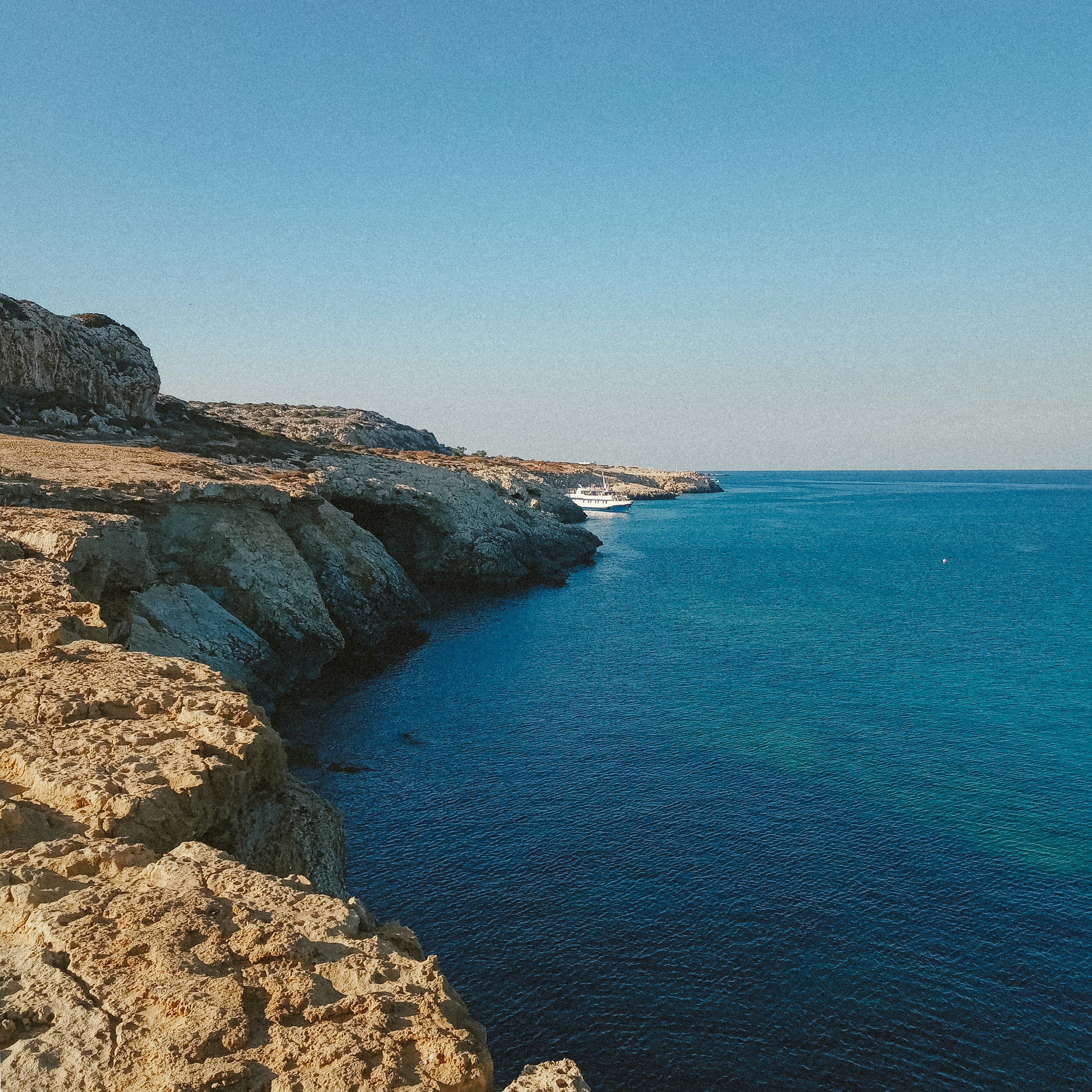 brown rocky mountain beside blue sea under blue sky during daytime