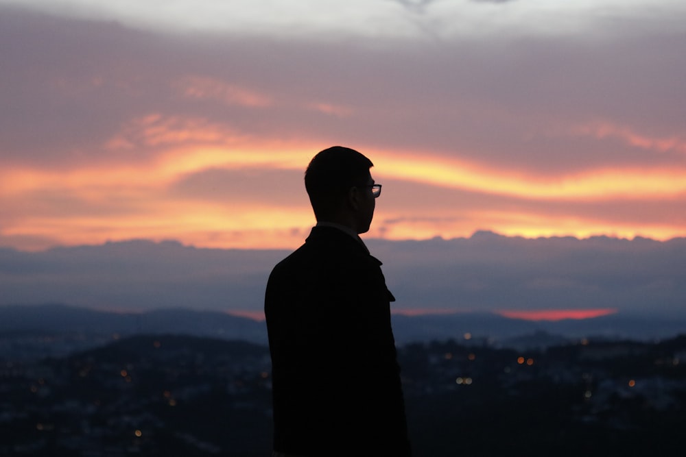 silhouette of man standing on top of mountain during sunset