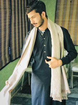 Man wearing a charcoal kameez shalwar standing against a minimalist off-white backdrop.