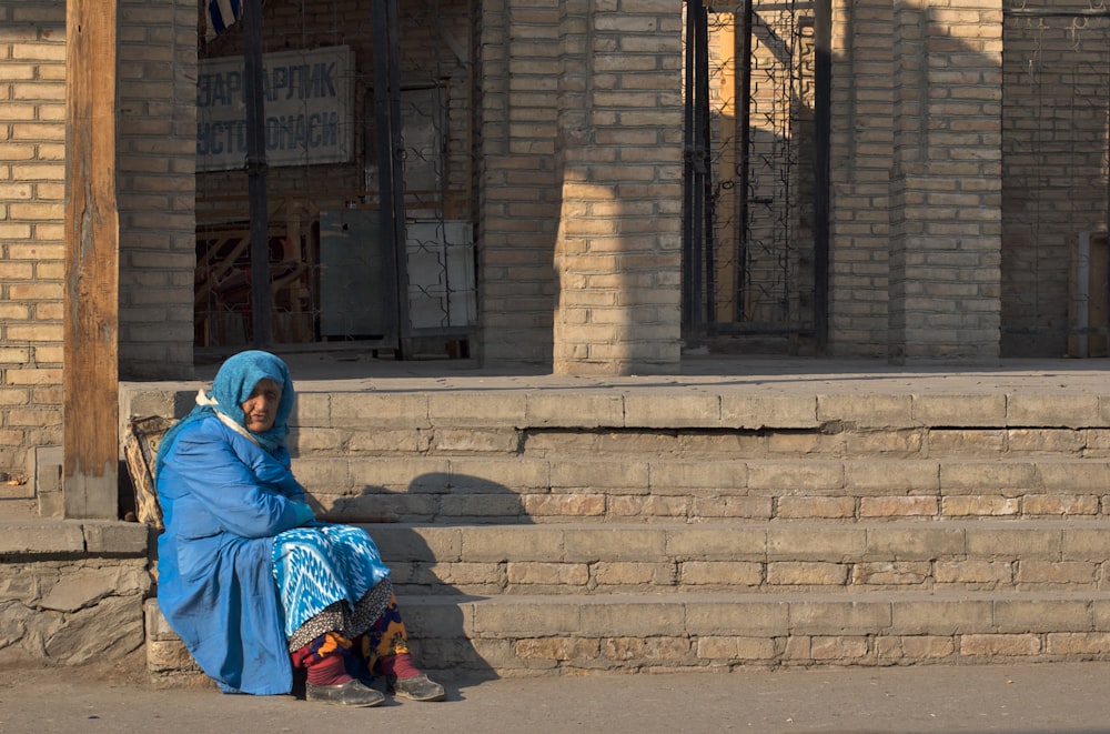 woman in blue hijab sitting on gray concrete stairs