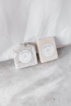 Two handcrafted soap bars are placed on a light, textured surface. Each bar has a round label with the words 'Eden Crafted' and a minimalist botanical illustration. The soaps appear to have natural, earthy tones and textures.