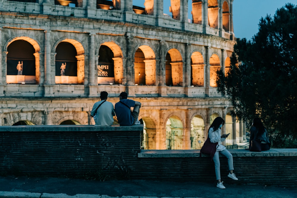 2 women sitting on bench in front of brown concrete building during daytime