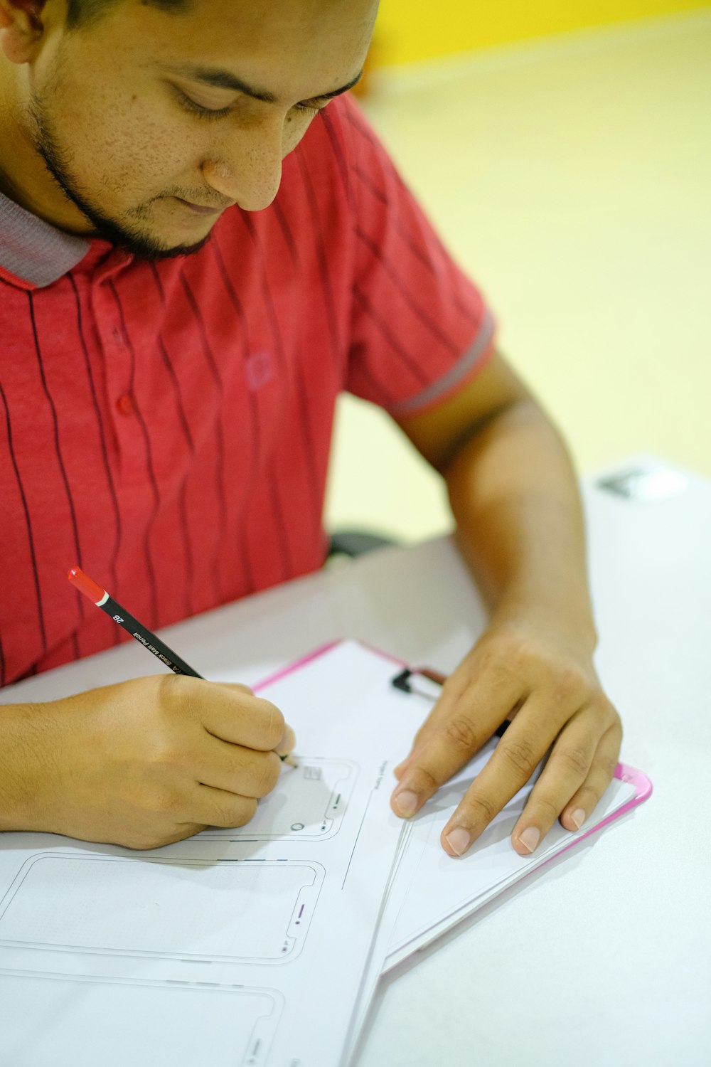 man in red crew neck t-shirt writing on white paper