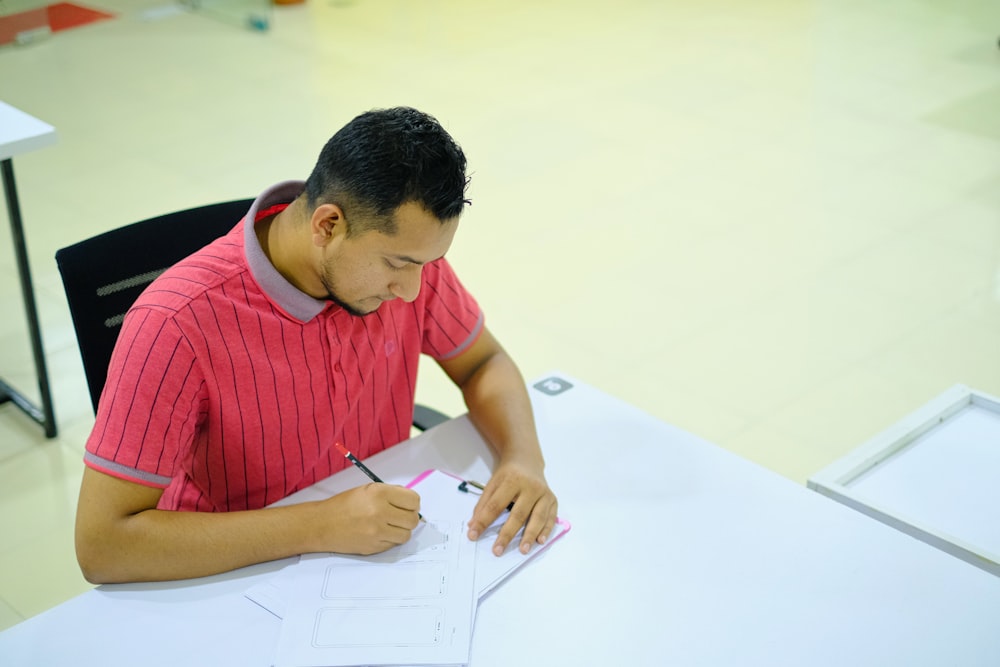 man in red and white striped crew neck t-shirt writing on white paper