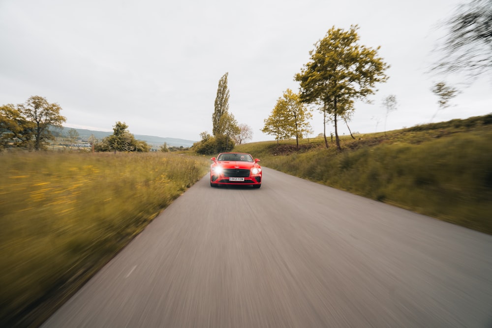 red car on road between green grass field during daytime