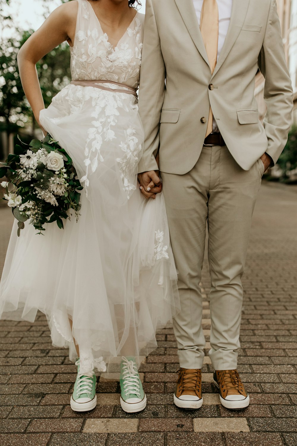 homme en veste de costume grise et femme en robe de mariée blanche tenant un bouquet de fleurs blanches