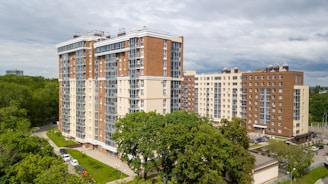 white and brown concrete building near green trees under white clouds during daytime