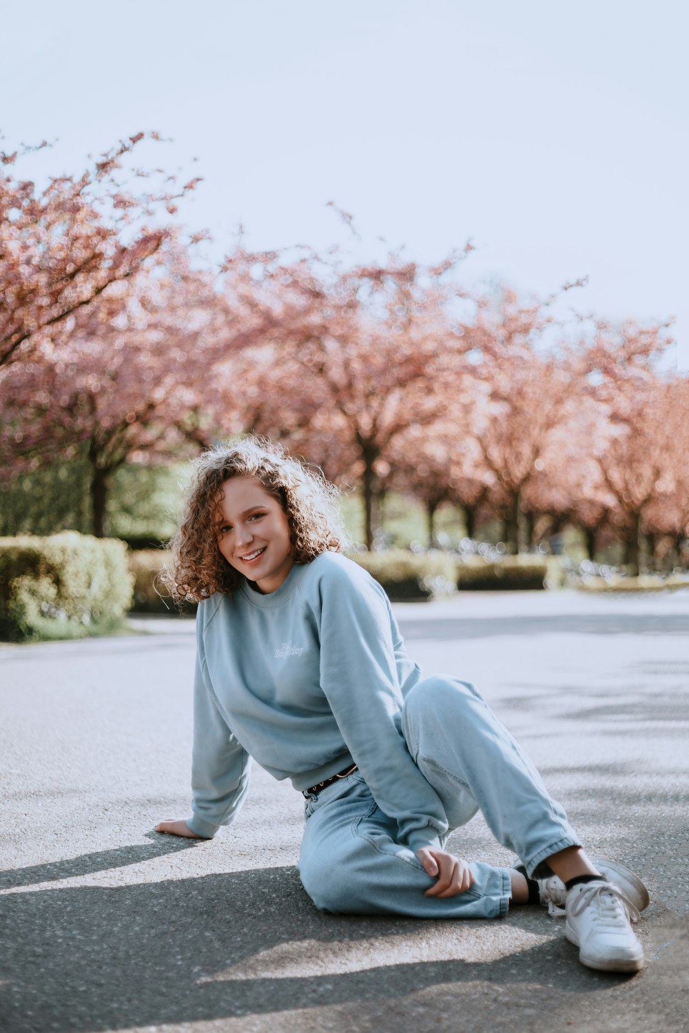 woman in gray sweater sitting on gray concrete road during daytime