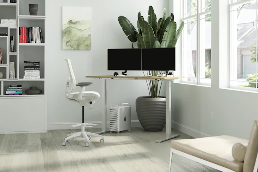 A serene, sunlit home office with minimalist decor and a tidy desk overlooking a small indoor plant.