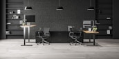 A modern office space with two workstations featuring adjustable desks and ergonomic chairs. The background includes a dark brick wall with symmetrical black shelves, adorned with minimalistic decor such as books, framed art, and plants. The lighting is provided by sleek pendant lamps.