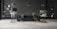 A modern office space with two workstations featuring adjustable desks and ergonomic chairs. The background includes a dark brick wall with symmetrical black shelves, adorned with minimalistic decor such as books, framed art, and plants. The lighting is provided by sleek pendant lamps.