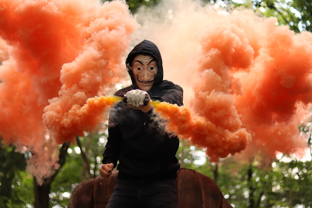 Mujer con chaqueta negra sosteniendo humo naranja