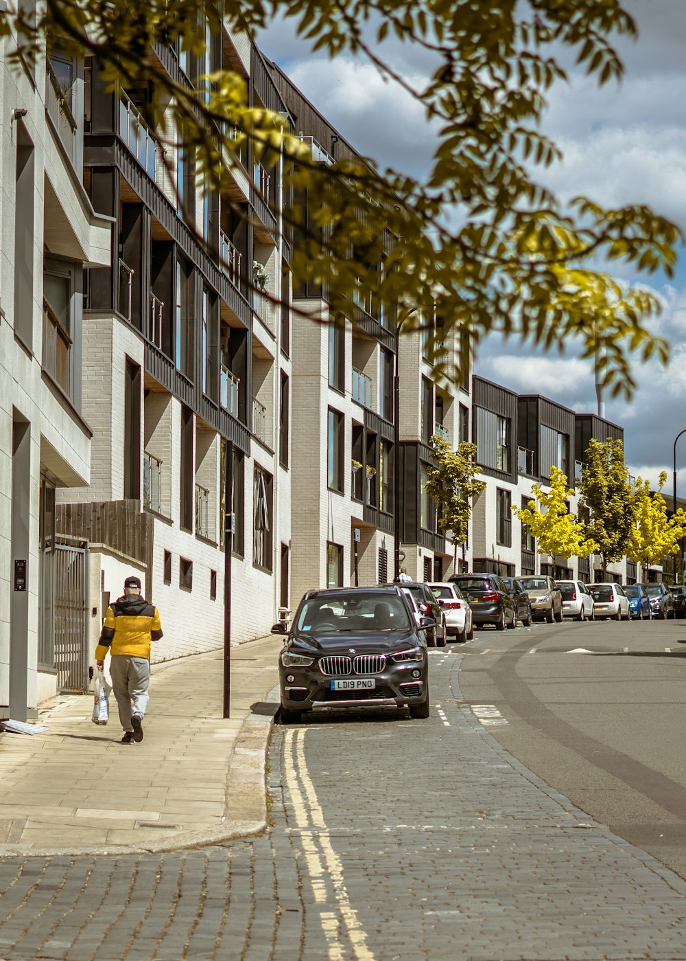 man in yellow jacket and black pants walking on pedestrian lane during daytime