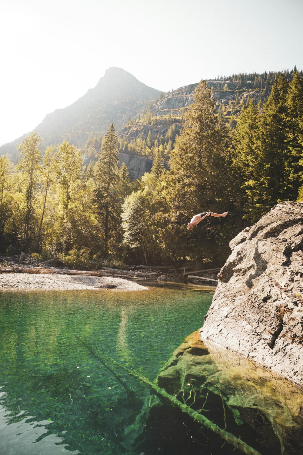person jumping on water near green trees and mountain during daytime