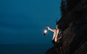 man in white shirt and black shorts standing on rock formation near body of water during