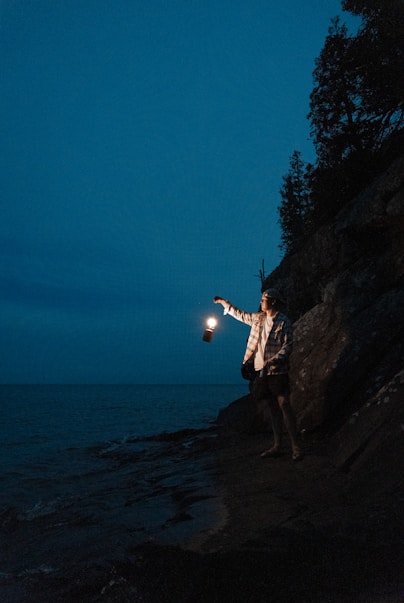 man in white shirt and black shorts standing on rock formation near body of water during