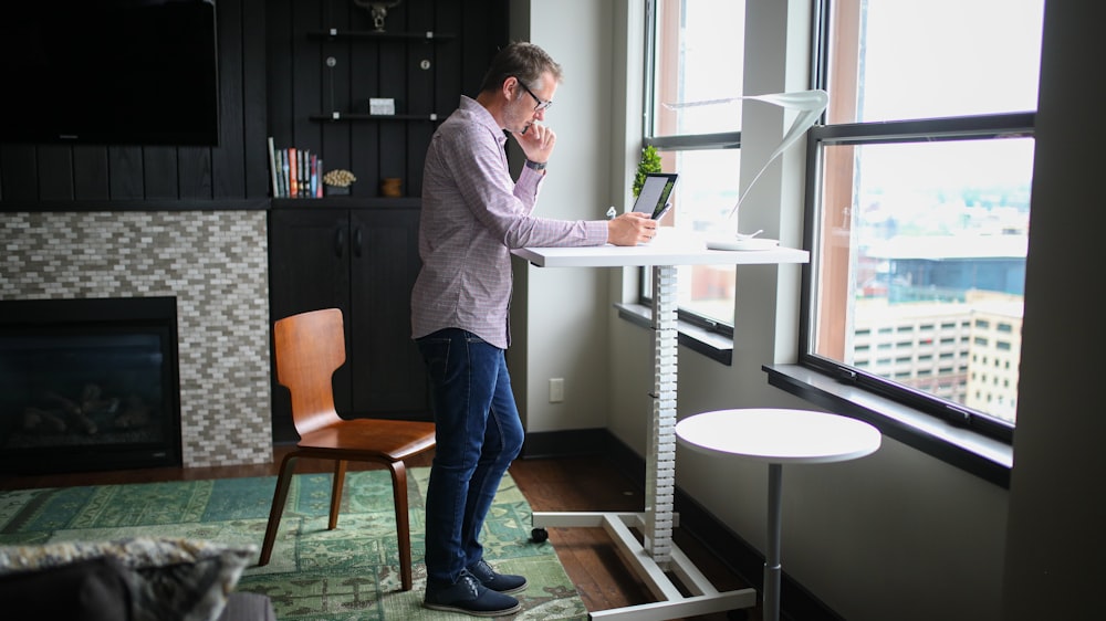 man in gray dress shirt and blue denim jeans standing beside white table