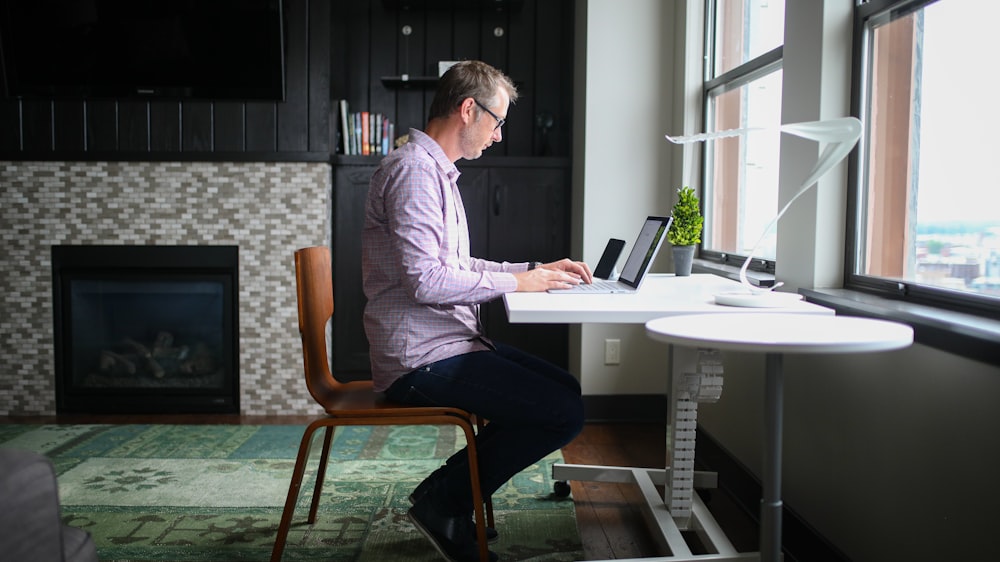 man in gray dress shirt sitting on brown wooden chair using macbook pro