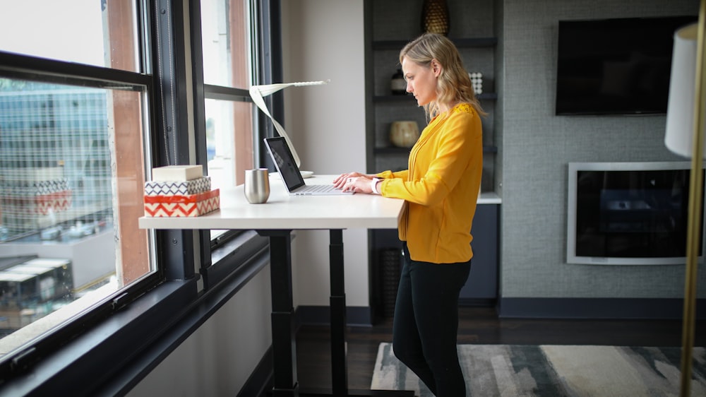 woman in yellow long sleeve shirt and black pants standing beside white table