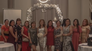A group of Spanish businesswomen smiling and chatting during a high-level meeting on a cruise ship deck with vibrant fuchsia and pink decorations.