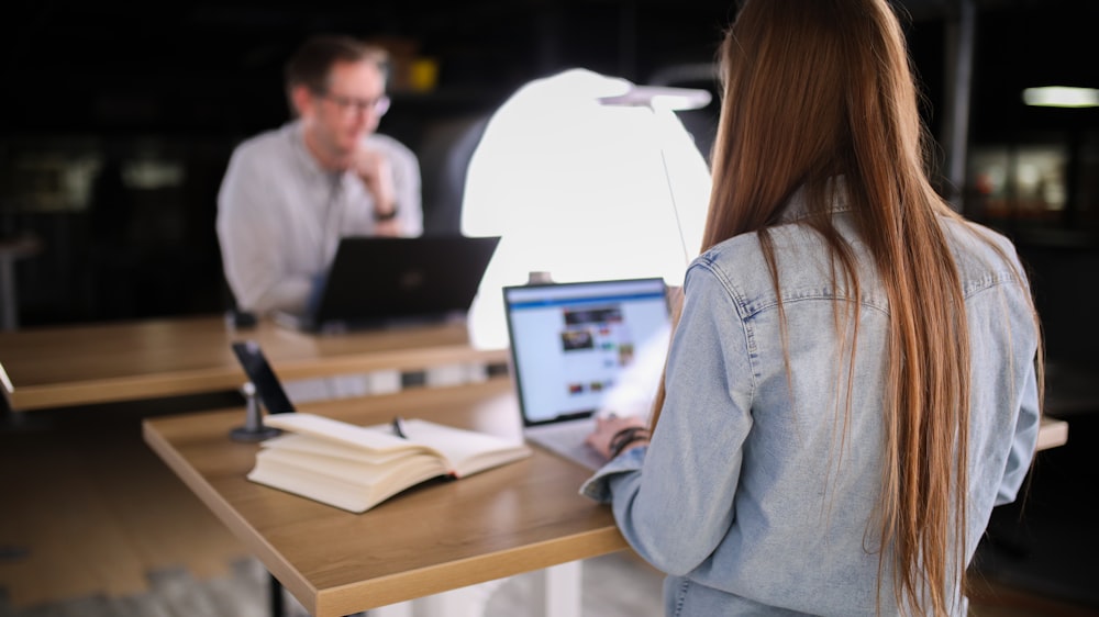 woman in blue denim jacket using macbook pro on brown wooden table