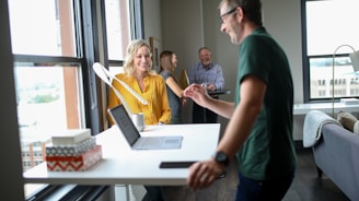 Four people in an office setting talking about work. A laptop on a cleaned desk next to clean window