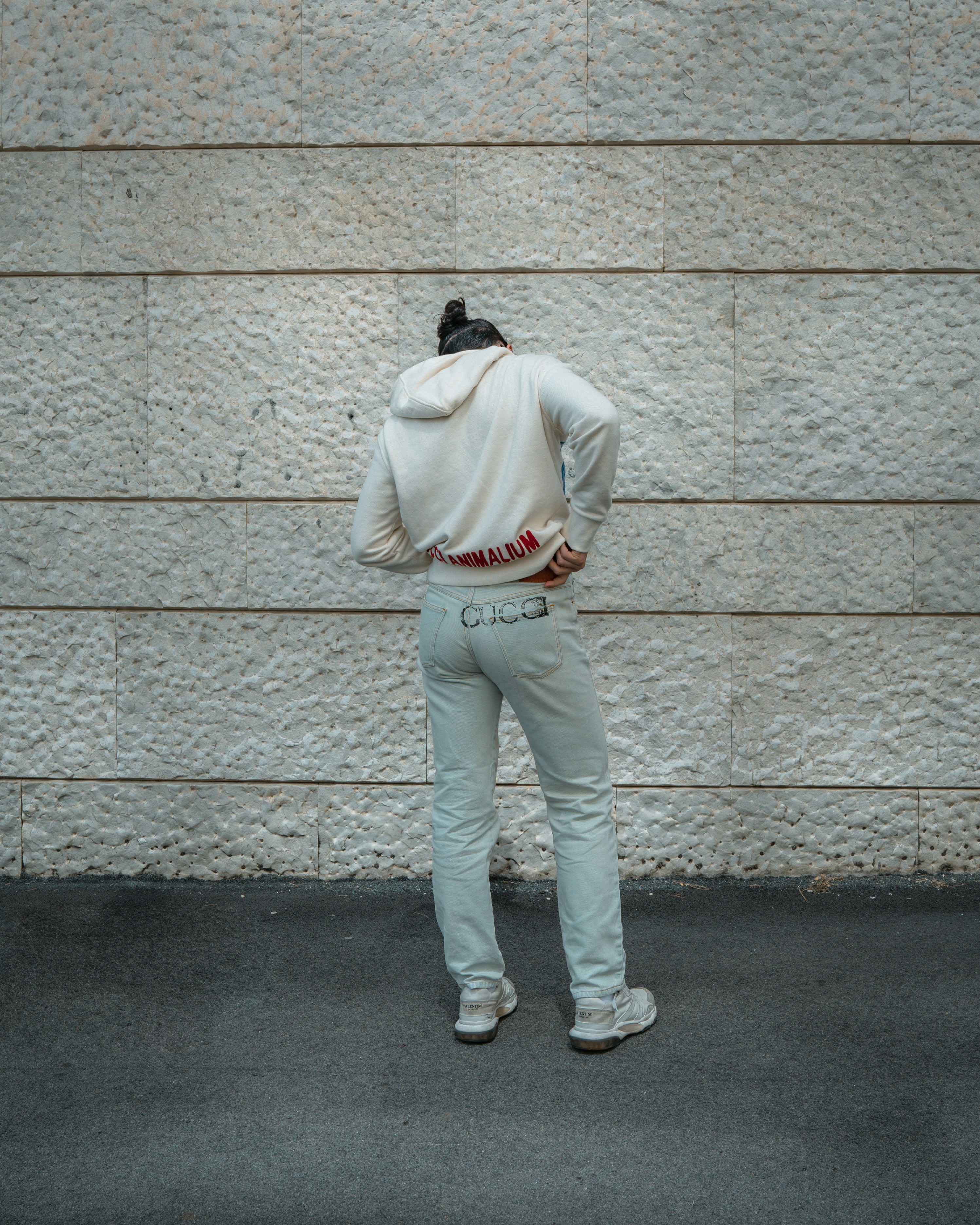 man in beige hoodie and white pants leaning on wall