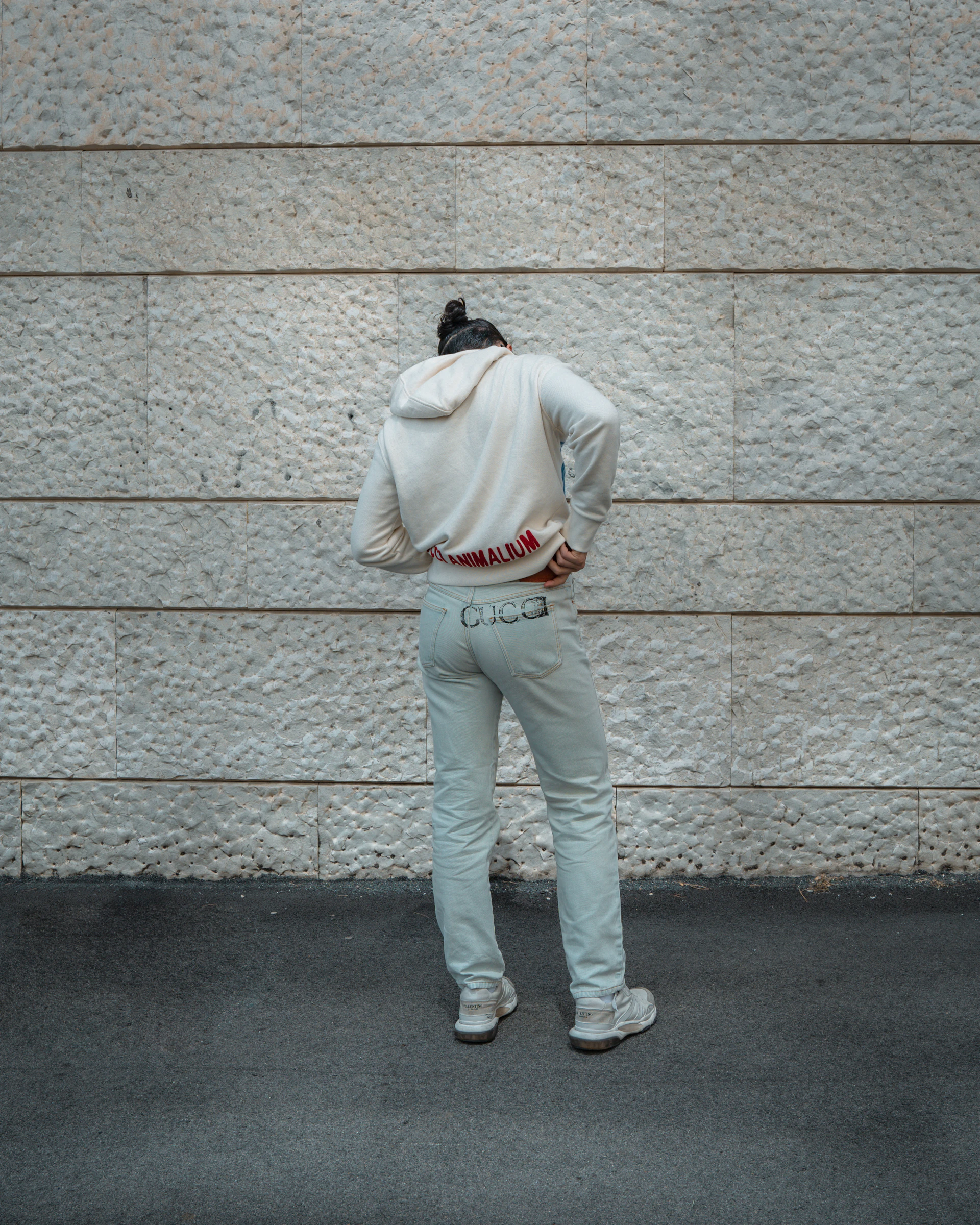 Hombre con polerón beige apoyado en un muro