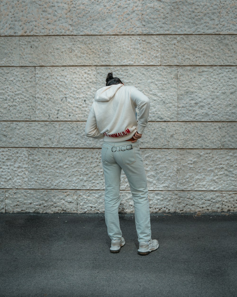man in beige hoodie and white pants leaning on wall