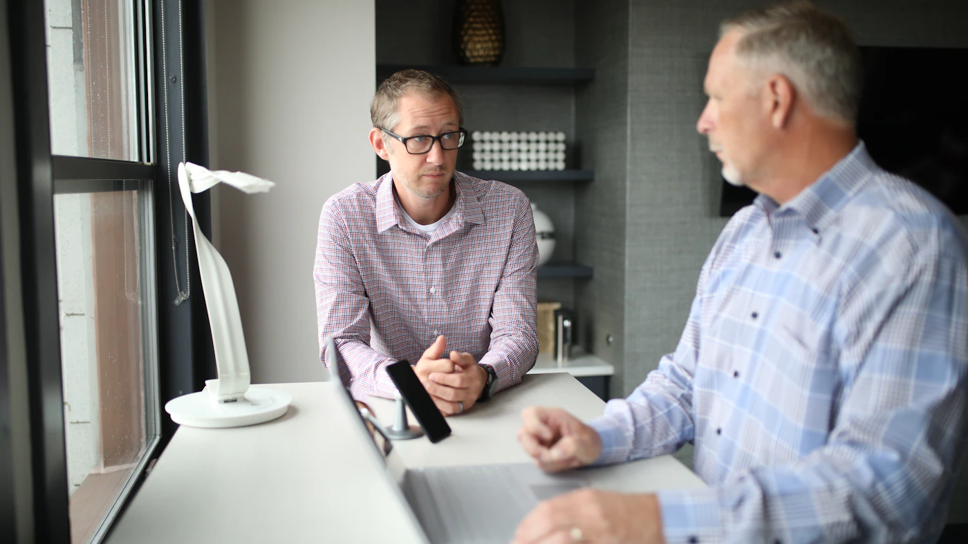 Two men talking across a desk in a bright office