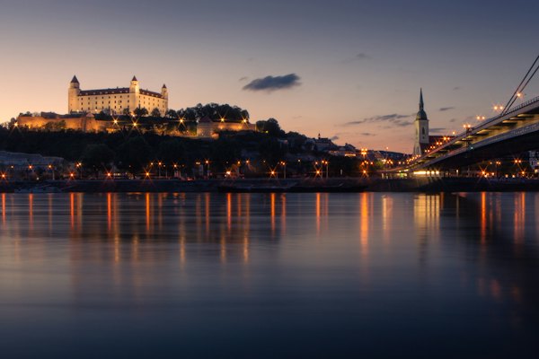 The castle lit up above the Danube at dusk — Bratislava, Slovakia