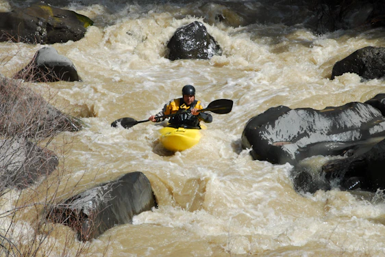 A kayaker navigating powerful whitewater rapids surrounded by rugged mountain scenery.