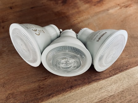 Three white LED light bulbs are arranged on a wooden surface. They feature a textured glass cover and are angled in different directions. The label on the side of one bulb reads, 'Philips'.