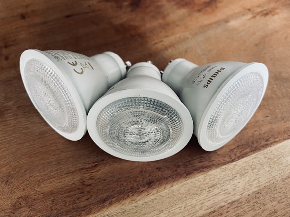 Three white LED light bulbs are arranged on a wooden surface. They feature a textured glass cover and are angled in different directions. The label on the side of one bulb reads, 'Philips'.