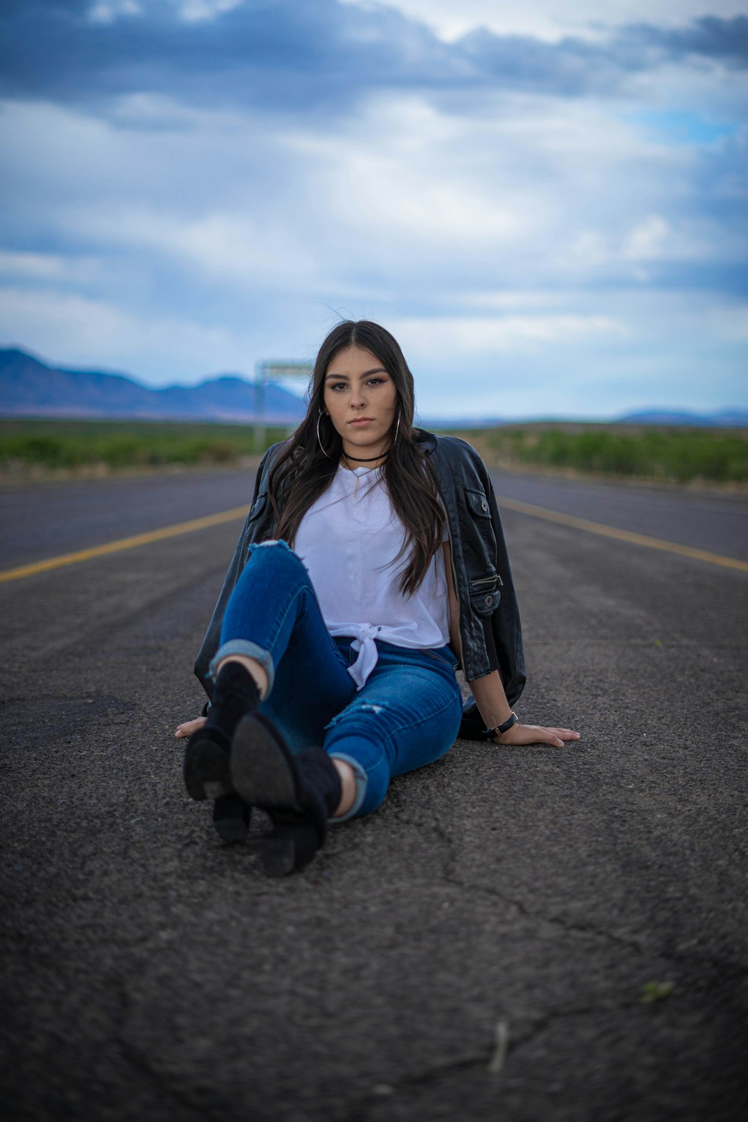 woman in white long sleeve shirt and blue denim jeans sitting on road during daytime