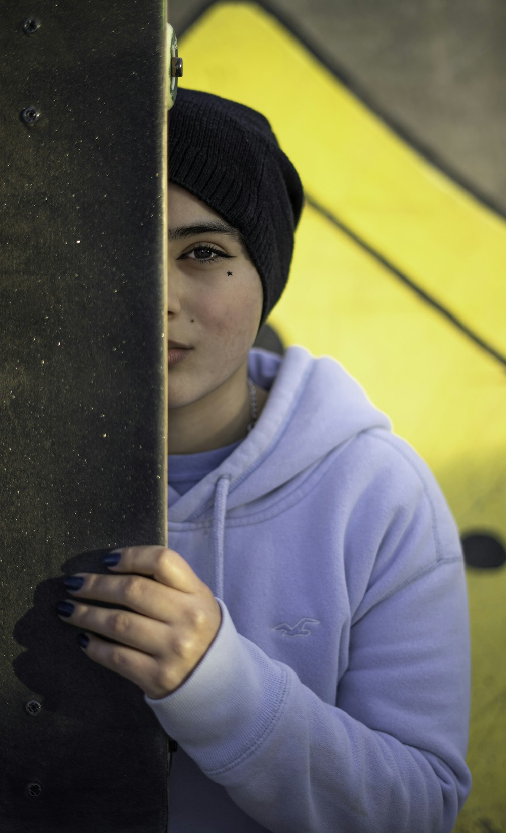 boy in blue hoodie and black knit cap holding black wooden panel