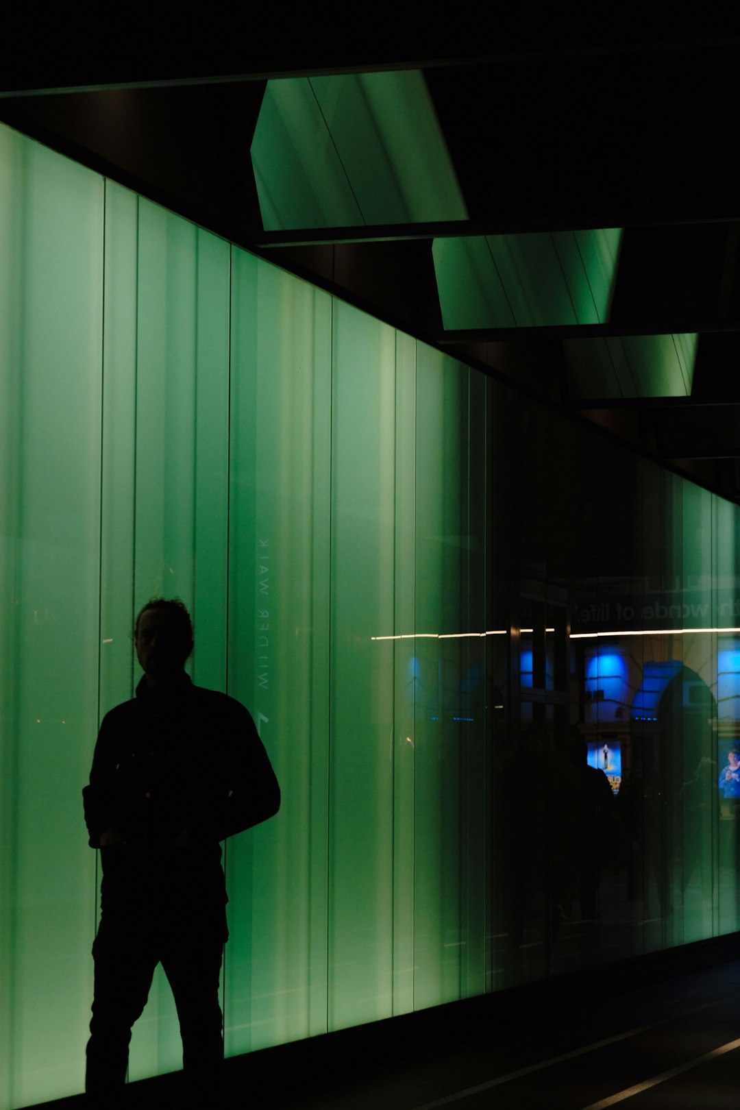 man in black jacket standing in front of green and white wall