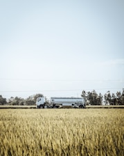 Water tanker truck driving through a rural landscape under a clear sky.