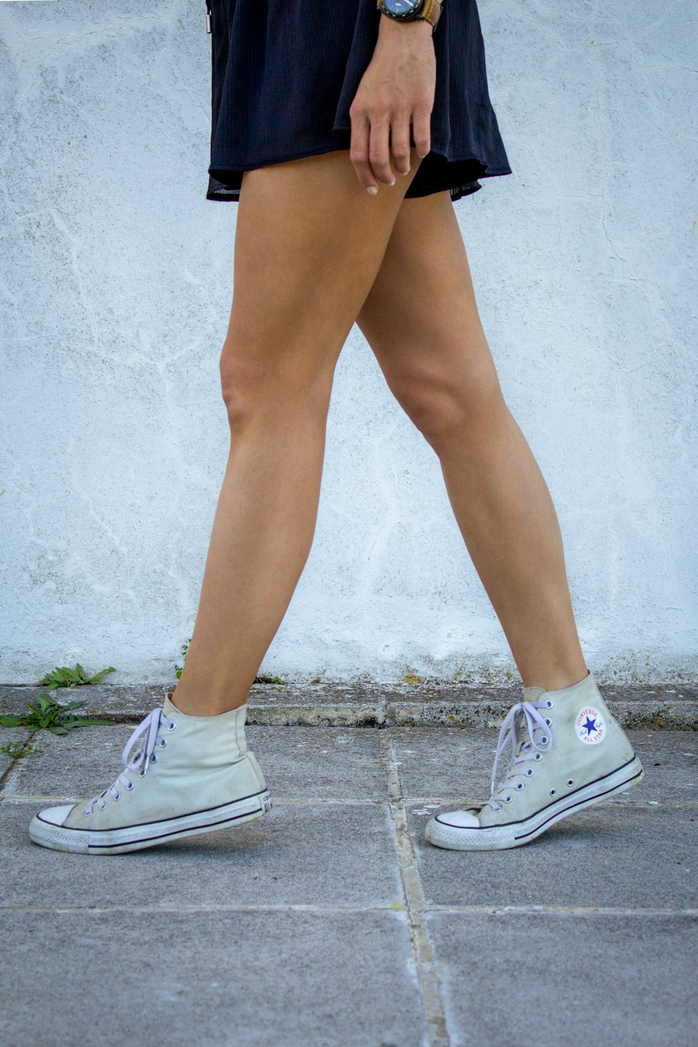 a woman walking down a sidewalk wearing tennis shoes