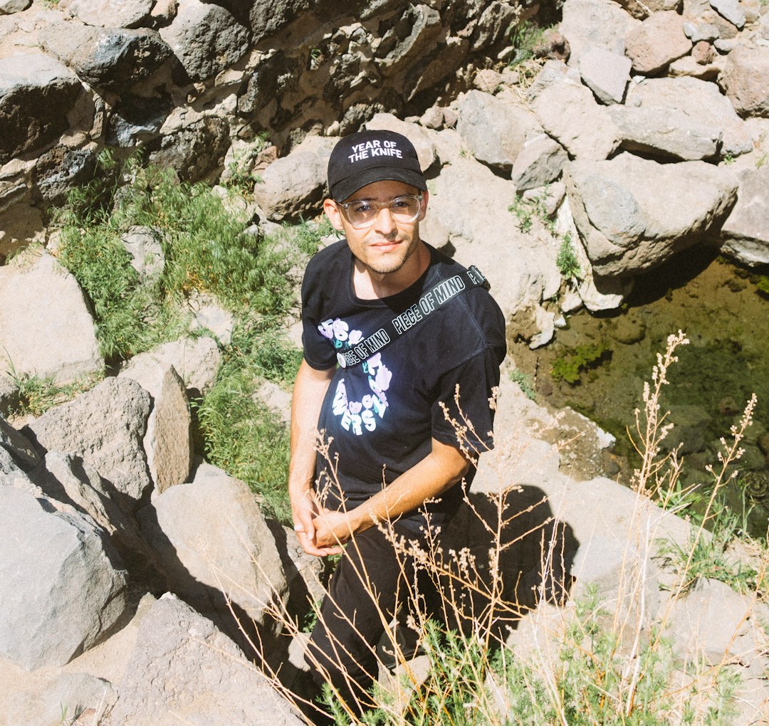 man in black crew neck t-shirt and black cap standing on rocky mountain during daytime