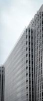 A tall, modern building with a grid-like exterior made of glass and metal. The building's design features numerous evenly spaced vertical and horizontal lines. The top part of the building displays the word 'BERLIN'. The sky in the background is overcast.