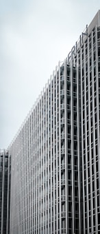 A tall, modern building with a grid-like exterior made of glass and metal. The building's design features numerous evenly spaced vertical and horizontal lines. The top part of the building displays the word 'BERLIN'. The sky in the background is overcast.