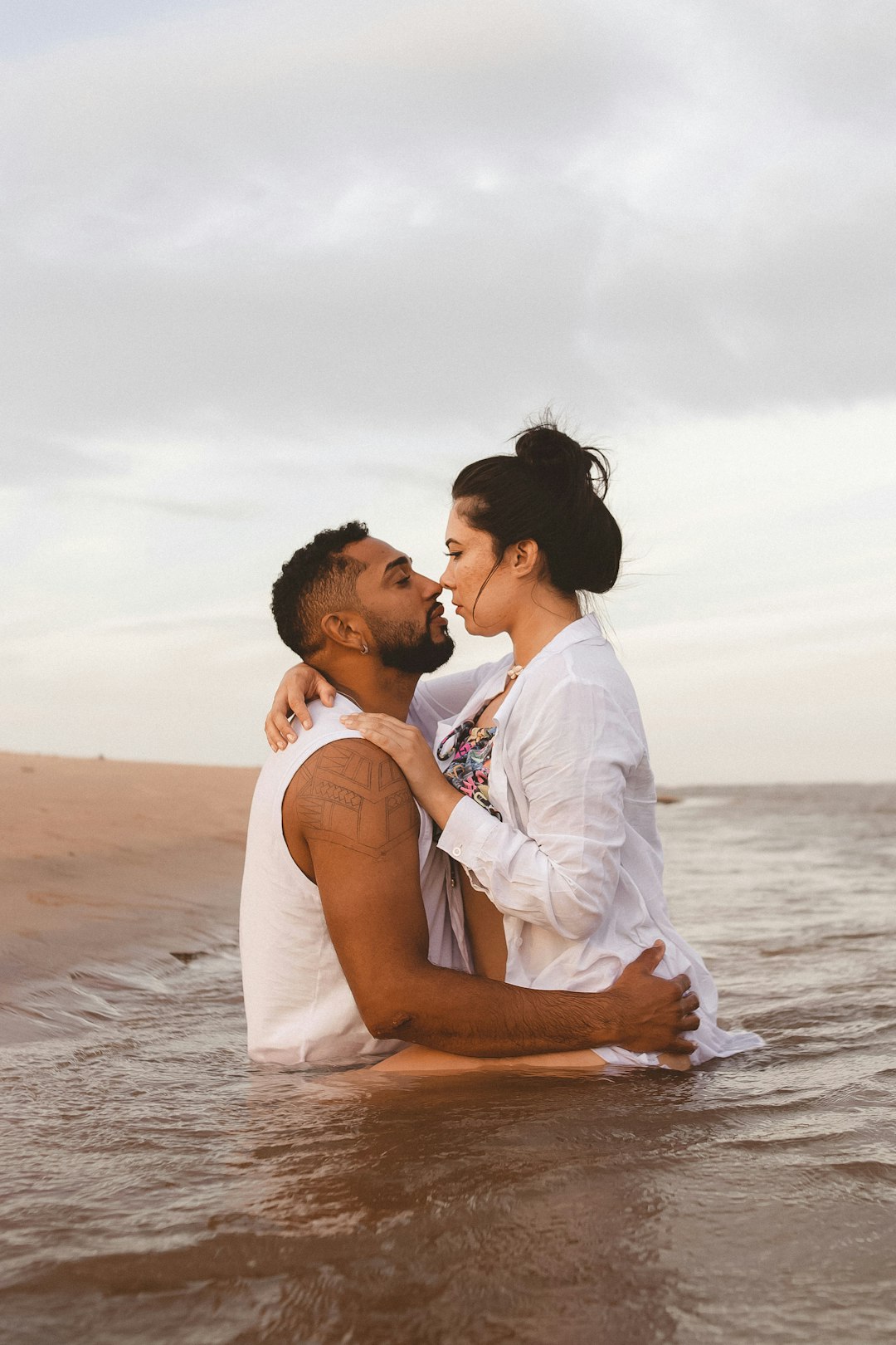 man in white dress shirt kissing woman in white dress on beach during daytime