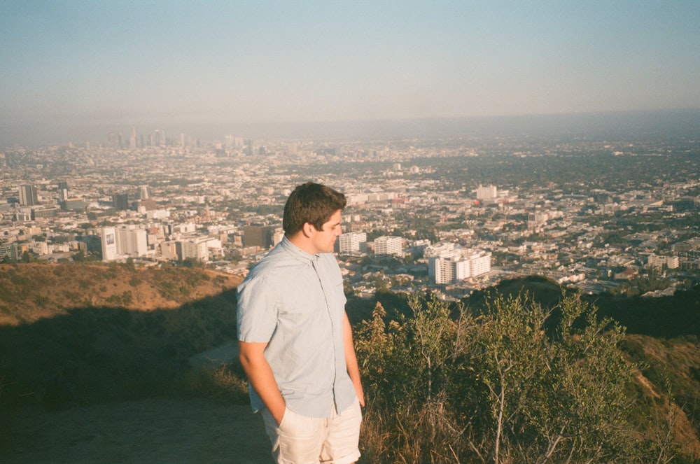 man in white t-shirt standing on top of the building looking at the city during