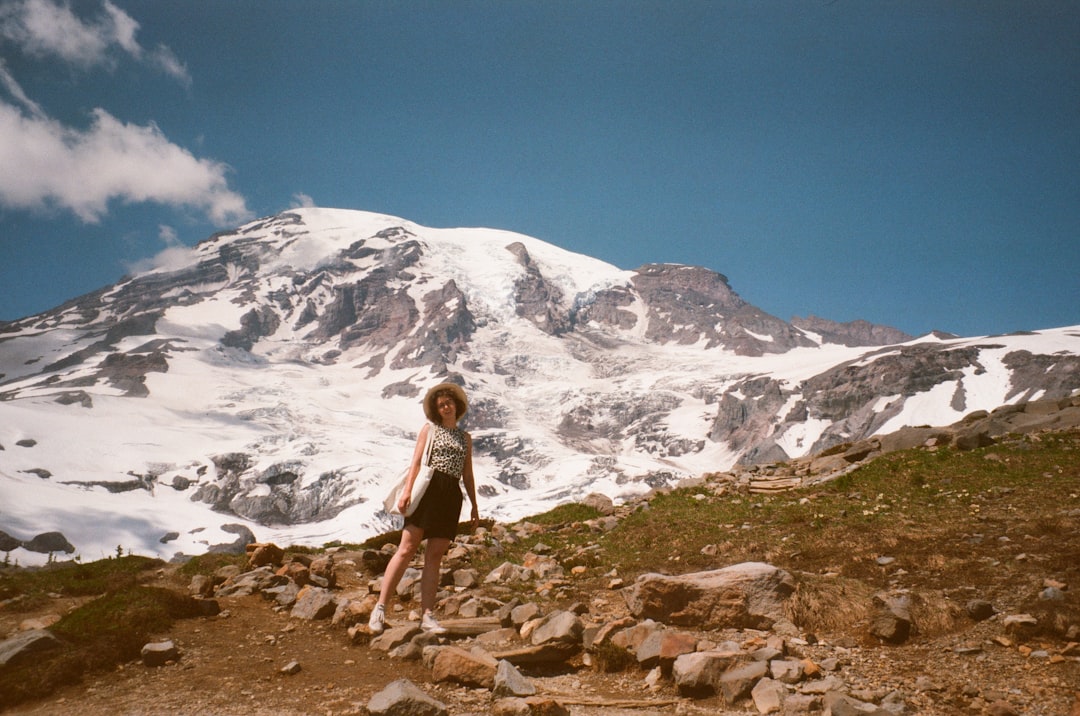 woman in black tank top and blue denim shorts standing on rocky ground near snow covered