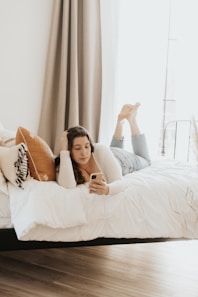 woman in pink long sleeve shirt lying on bed just playing on her phone.