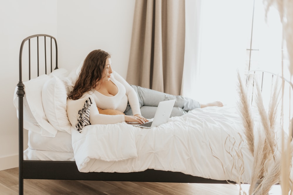 woman in white tank top lying on bed using macbook