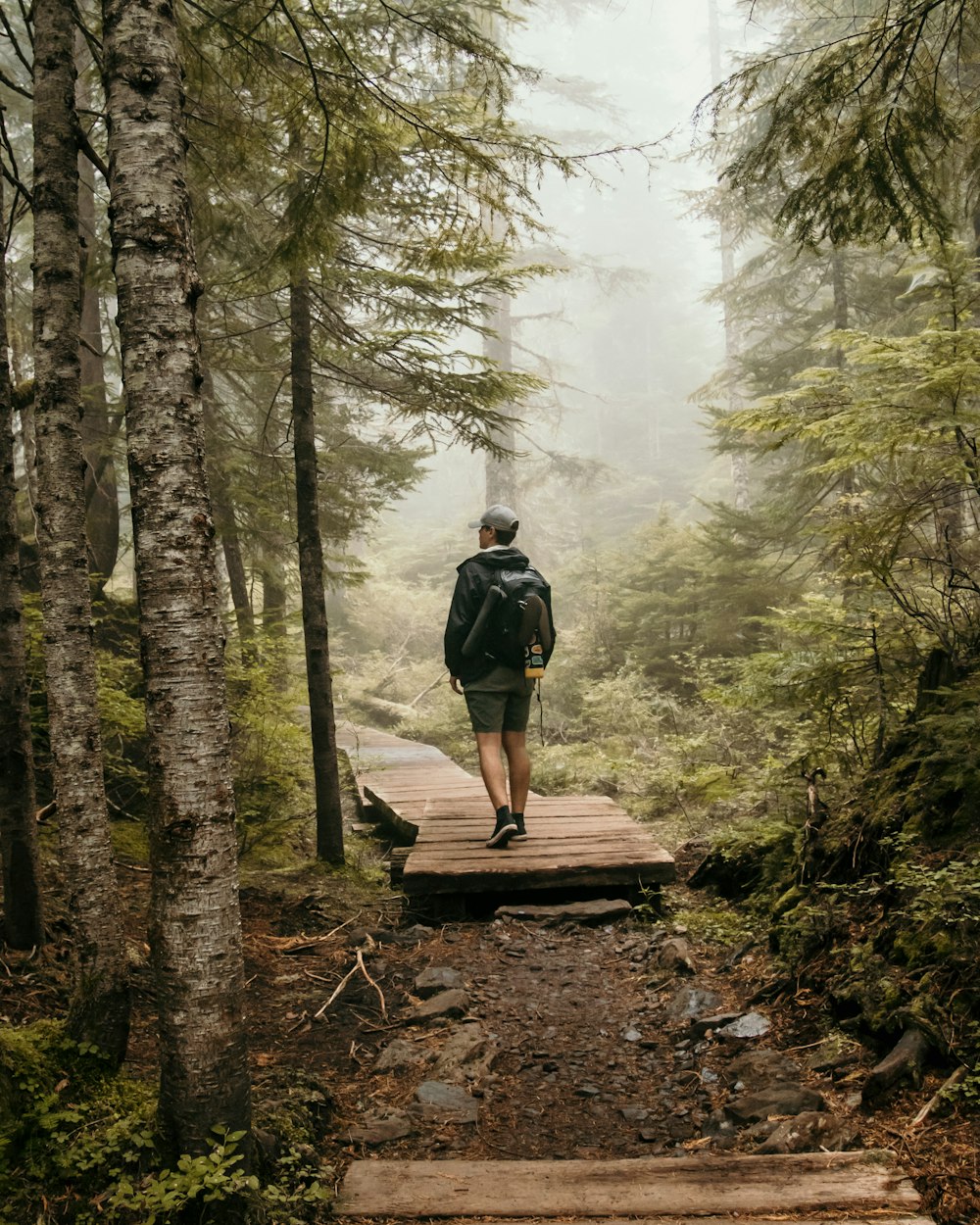 man in black backpack walking on brown wooden bridge in forest during daytime