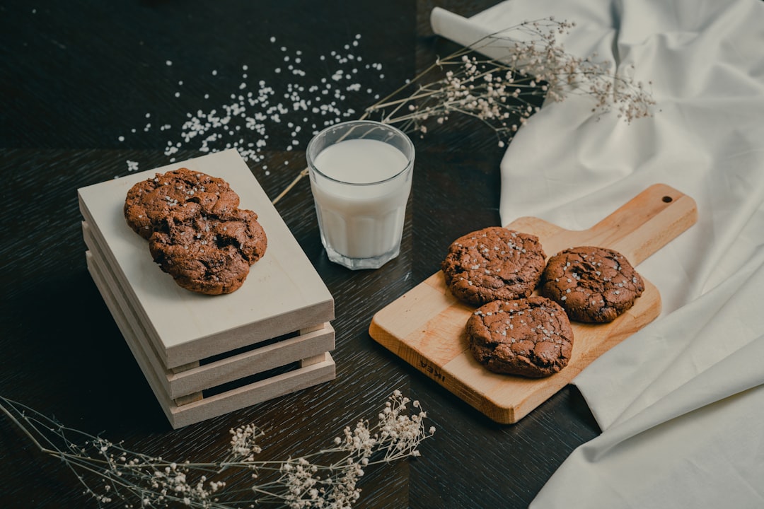 chocolate cookies on brown wooden tray beside clear drinking glass with milk