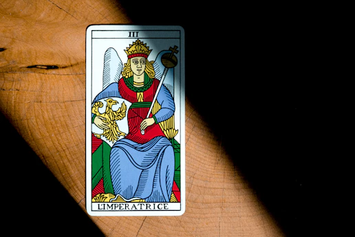 A detailed illustration of The Emperor tarot card, featuring a regal figure seated on a stone throne adorned with ram motifs, symbolizing authority and stability.